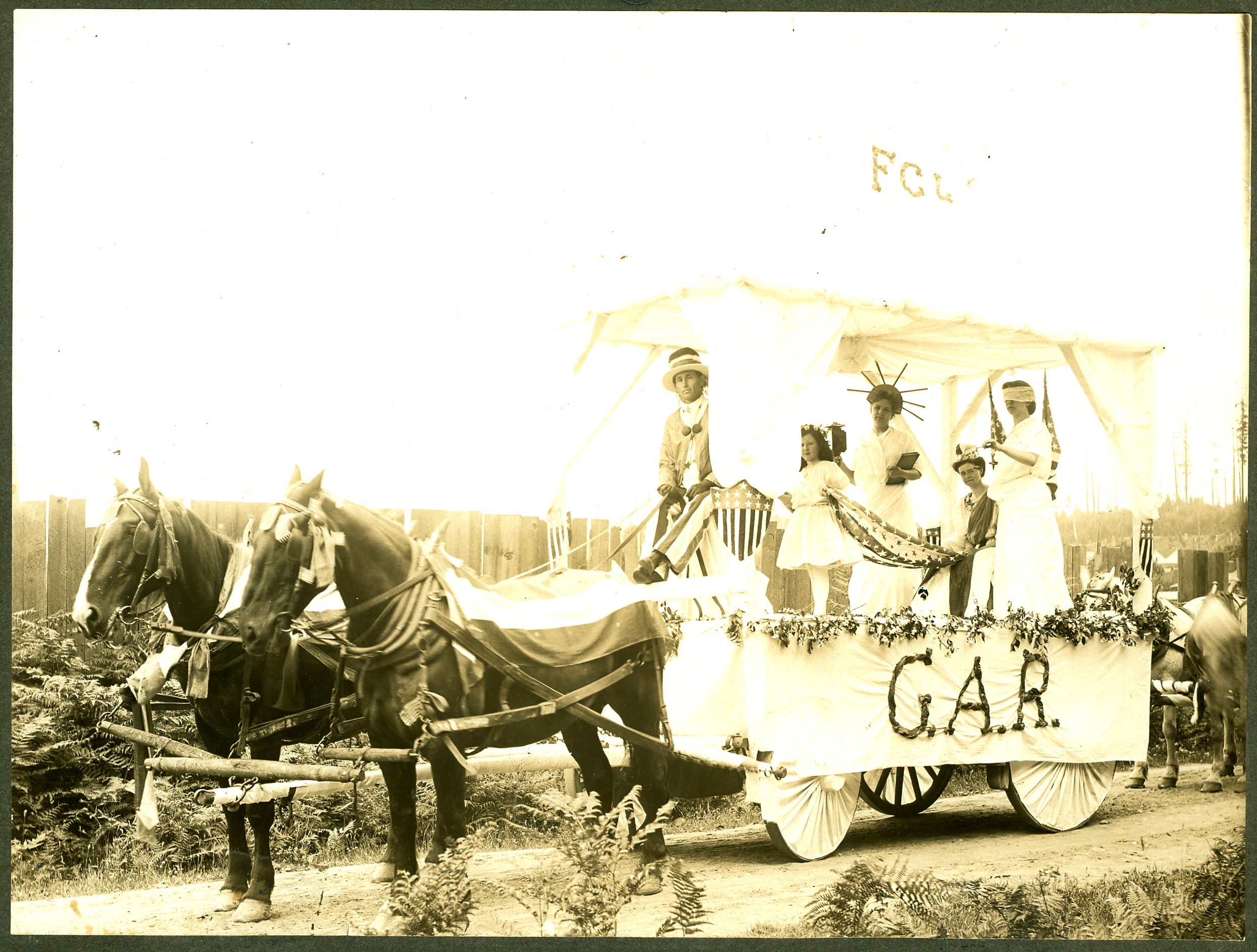 This G.A.R. float was designed by the Women's Relief Corps for the 1908 Bothell 4th of July Parade. Left to right on the float: depicting liberty, justice (blindfolded) and American independence (behind the unidentified driver) are Gladys Hannan, Hannah Staples as Liberty, Alta Elliot and a blindfolded Marie Campbell as Justice. The letters G.A.R. stood for Grand Army of the Republic, a reference to the U.S. Army (the North) during the Civil War. The G.A.R. fraternal organization was a veterans' group and included the Women's Relief Corps, their auxiliary unit. 