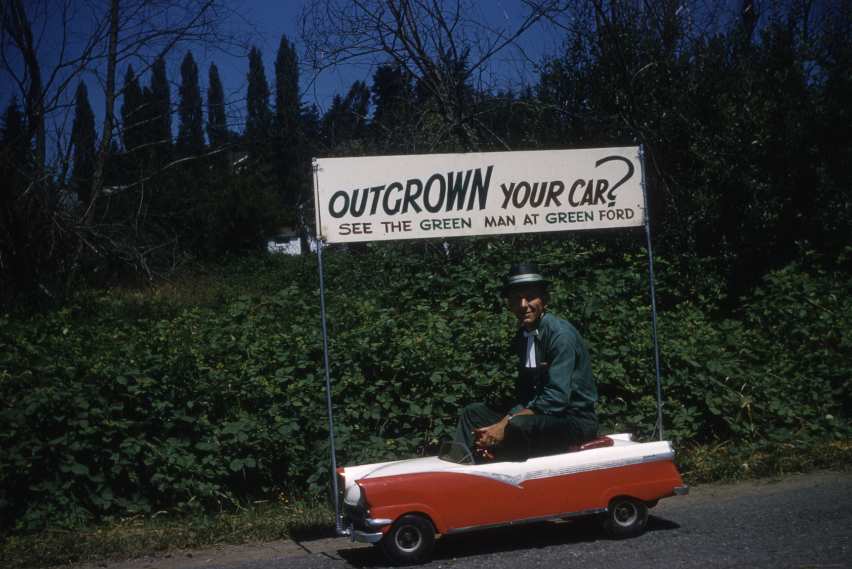 Promoting his car dealership, Green Ford, second-generation owner Ron Green rides in a scale model of a a 1956 Ford convertible. His father began the business as Green's Garage in 1919, changing the name to Green Motor Co. in 1930. After 1954, under Ron Green's ownership, it became Green Ford until its sale to Tom Chapman in 1965.