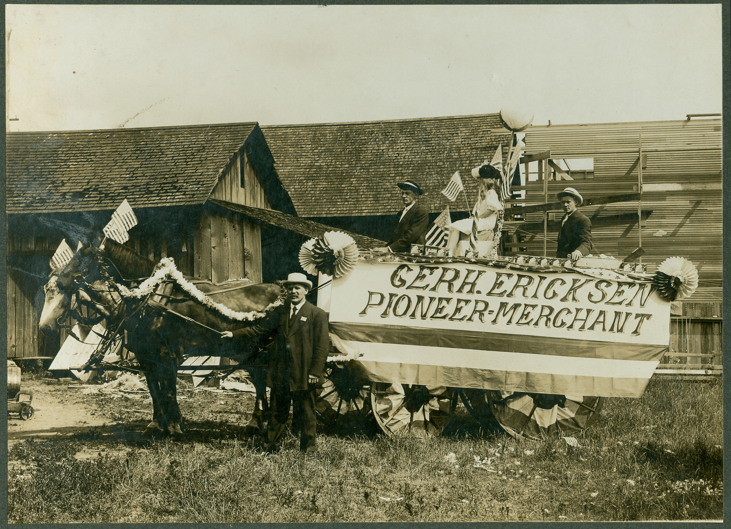 The Bothell July 4th parade float for Gerhard Ericksen's Mercantile Store on Main Street. The sign on the side of the float reads "Gerh. Ericksen Pioneer Merchant." Background for the picture is not identified. Those in the picture, according to a caption on the back of the photo, are left to right, Gerhard Ericksen, driver Lars Eidbo, unidentified person, and George Ericksen (Gerhard's son).