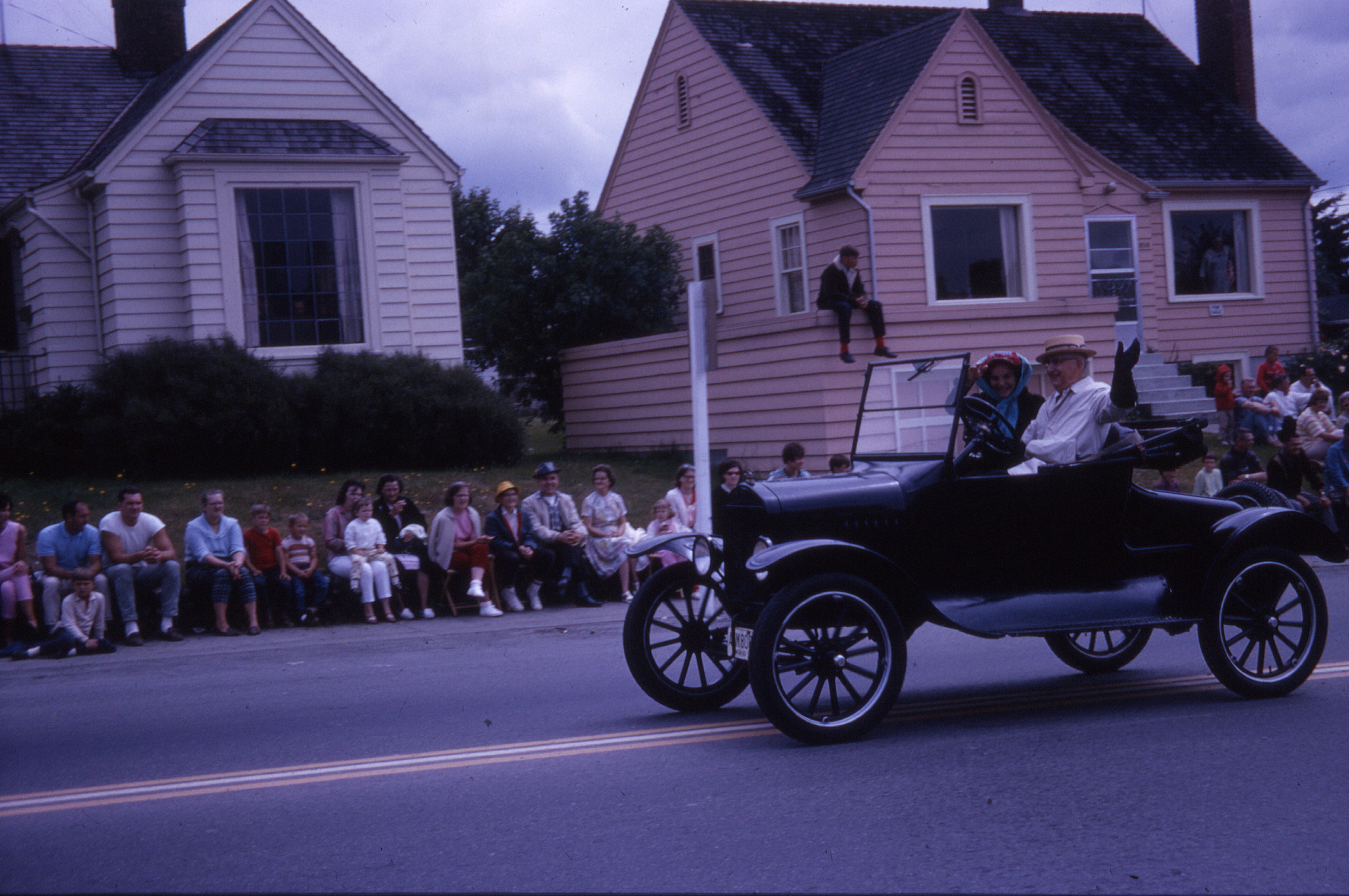 Near the start of the parade on Main Street, Charles Green drives his Model T Ford with passenger Ursula Hölscher, an exchange student from Krefeld-Uerdingen in Germany. Charles Green was a Ford dealer in Bothell from 1919 until selling the business to his son in 1954.